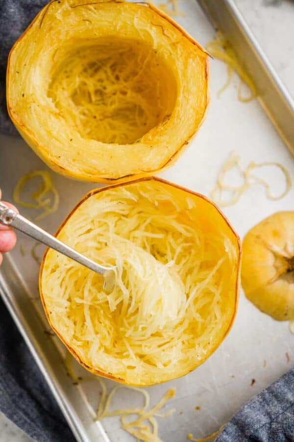 fork pulling up roasted spaghetti squash strands from squash half on baking sheet
