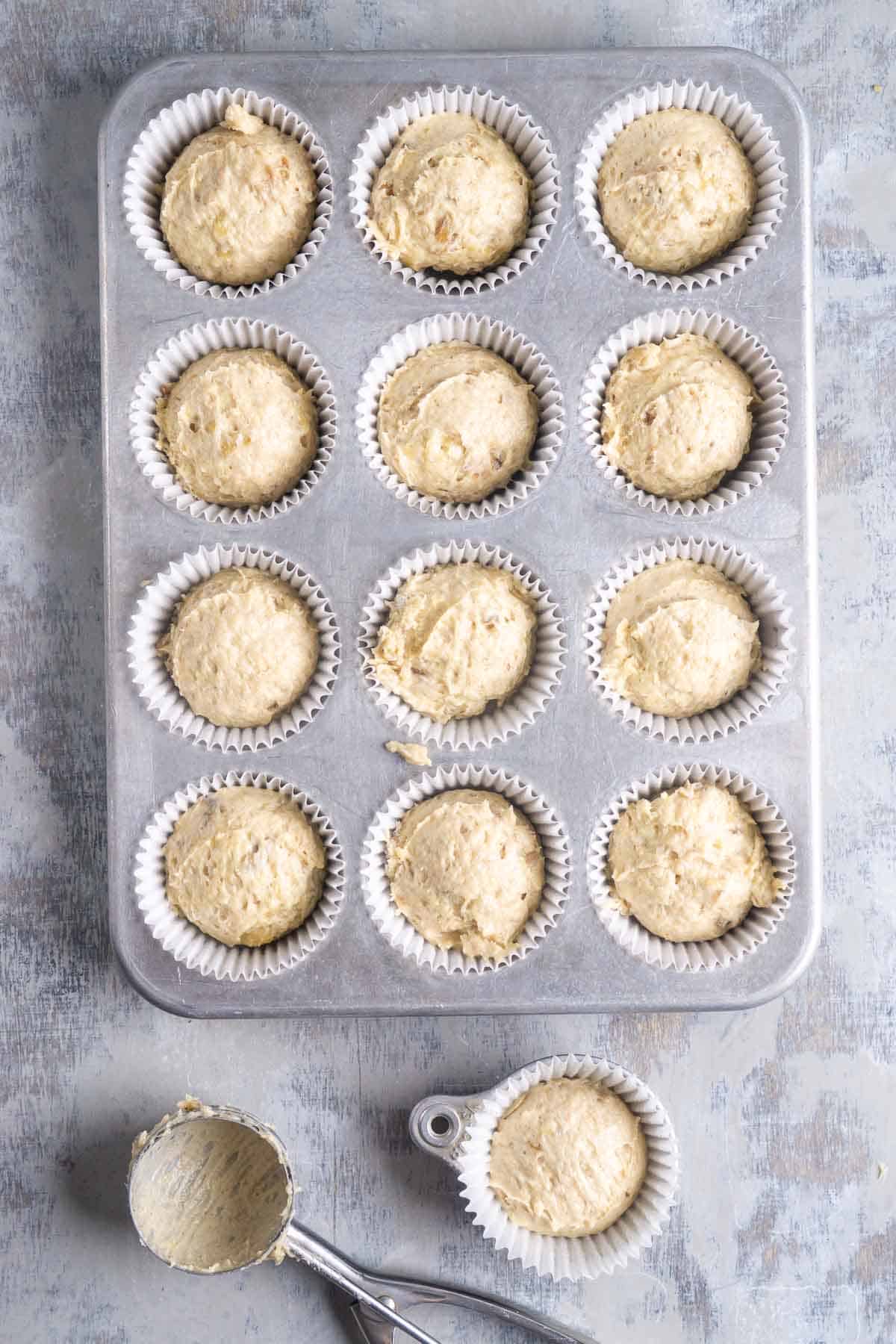 Banana bread muffin batter in lined muffin tin next to portion scoop