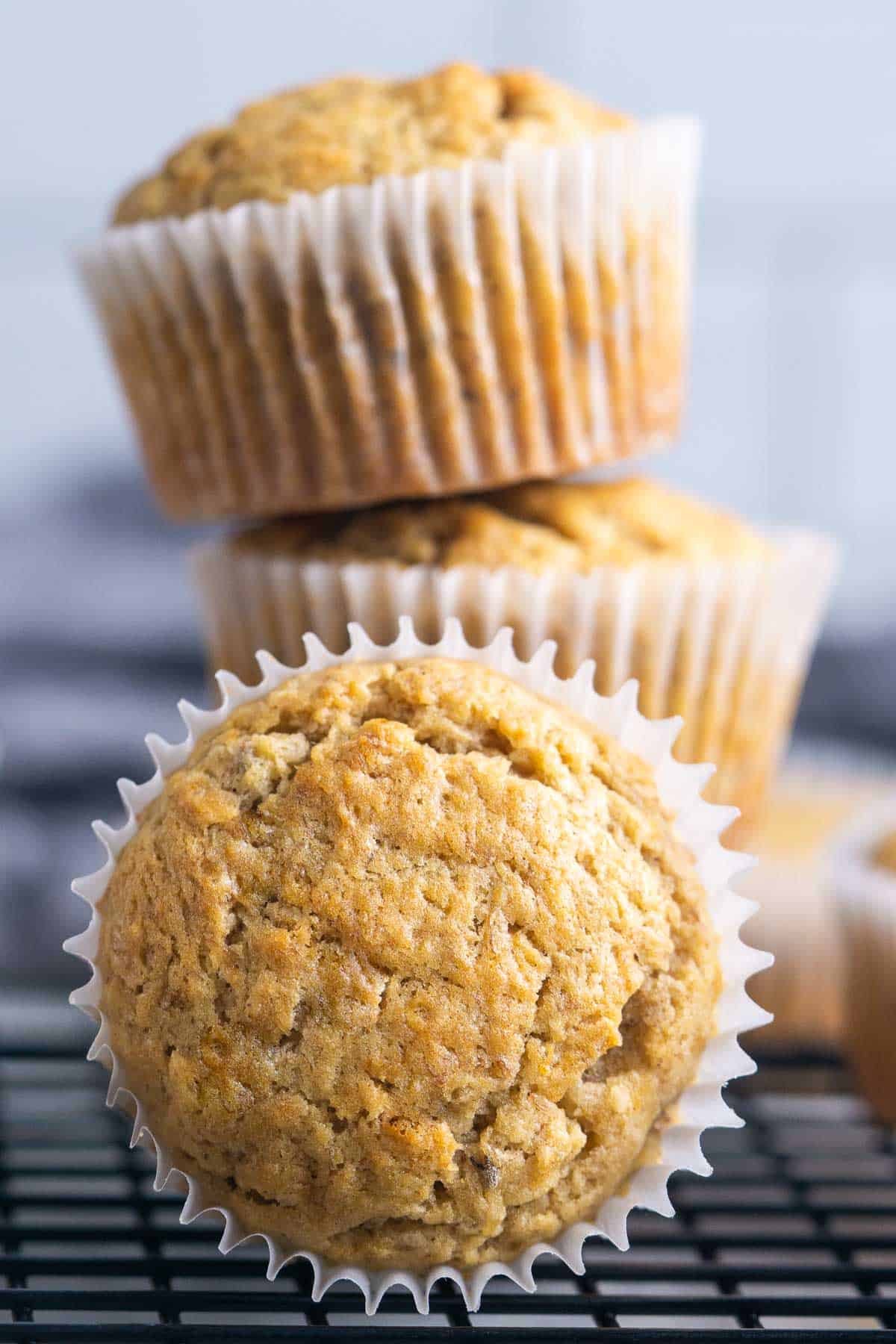 baked banana bread muffins in cupcake liners stacked on black cooling rack