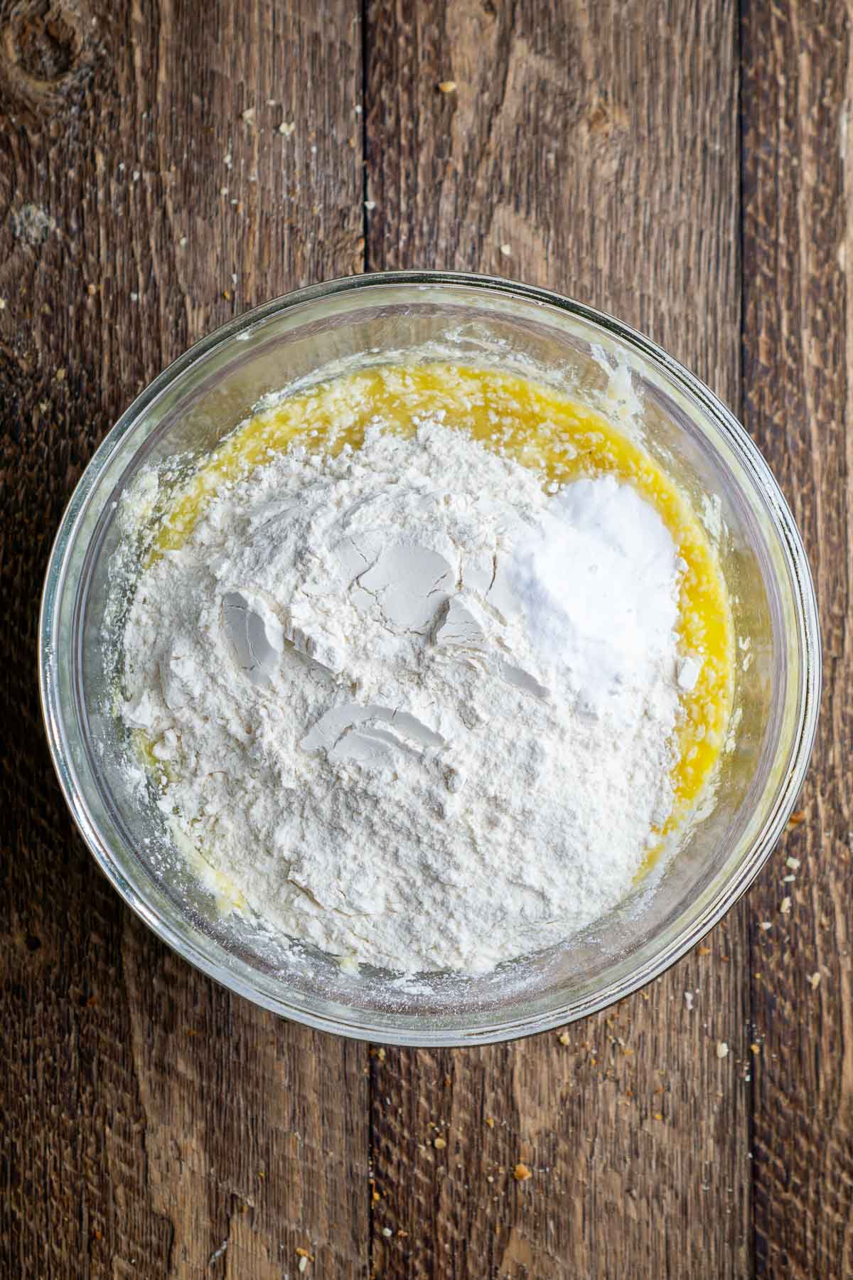 Flour sits on top of wet yellow mixture in a glass bowl.