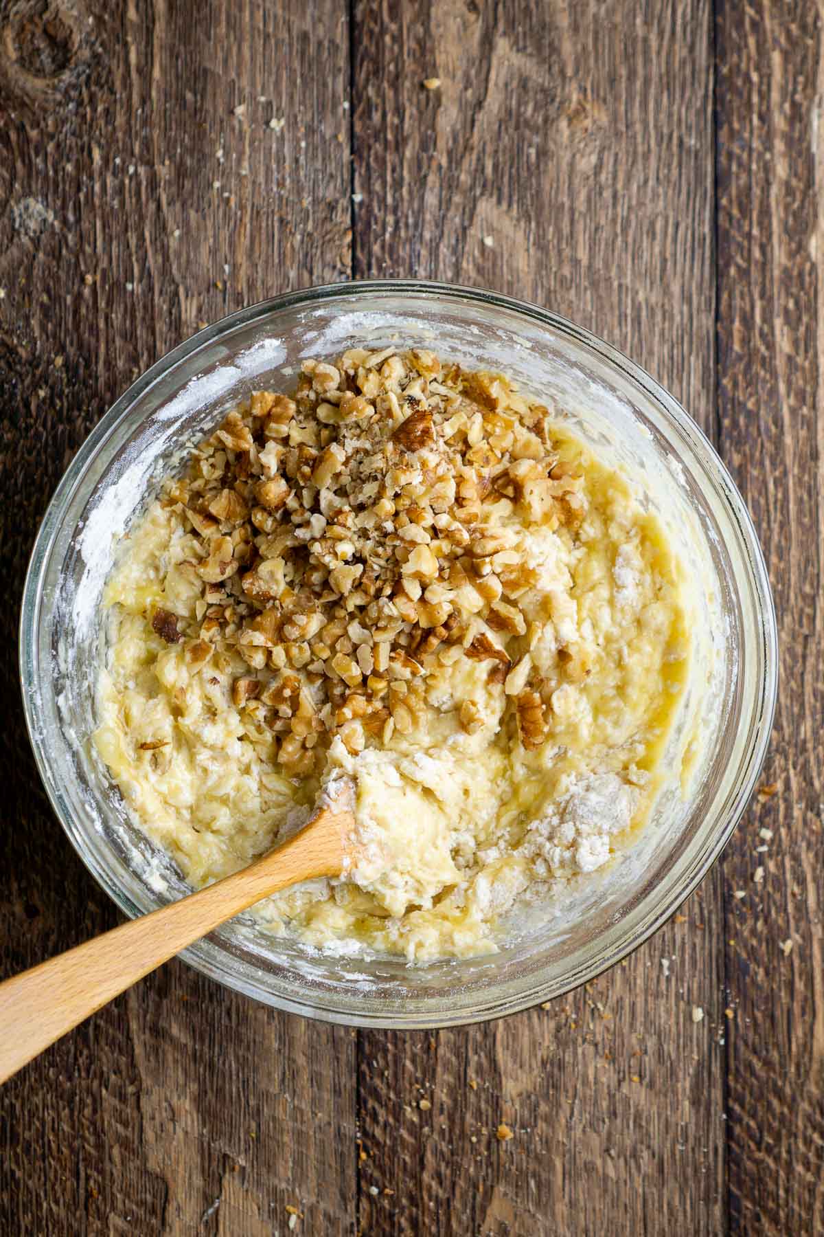 Partially mixed yellow batter with a pile of walnuts on top in a glass bowl.