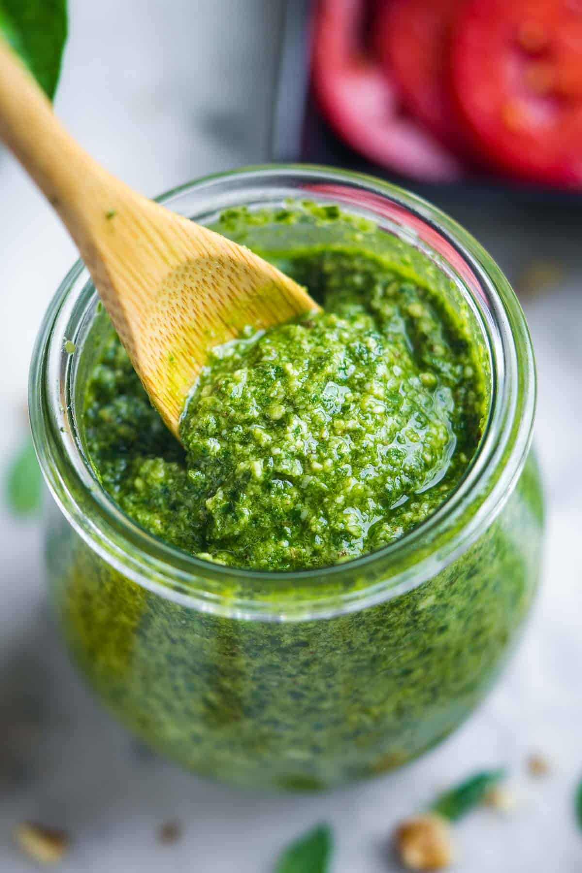 wooden spoon scooping basil pesto from a glass jar.