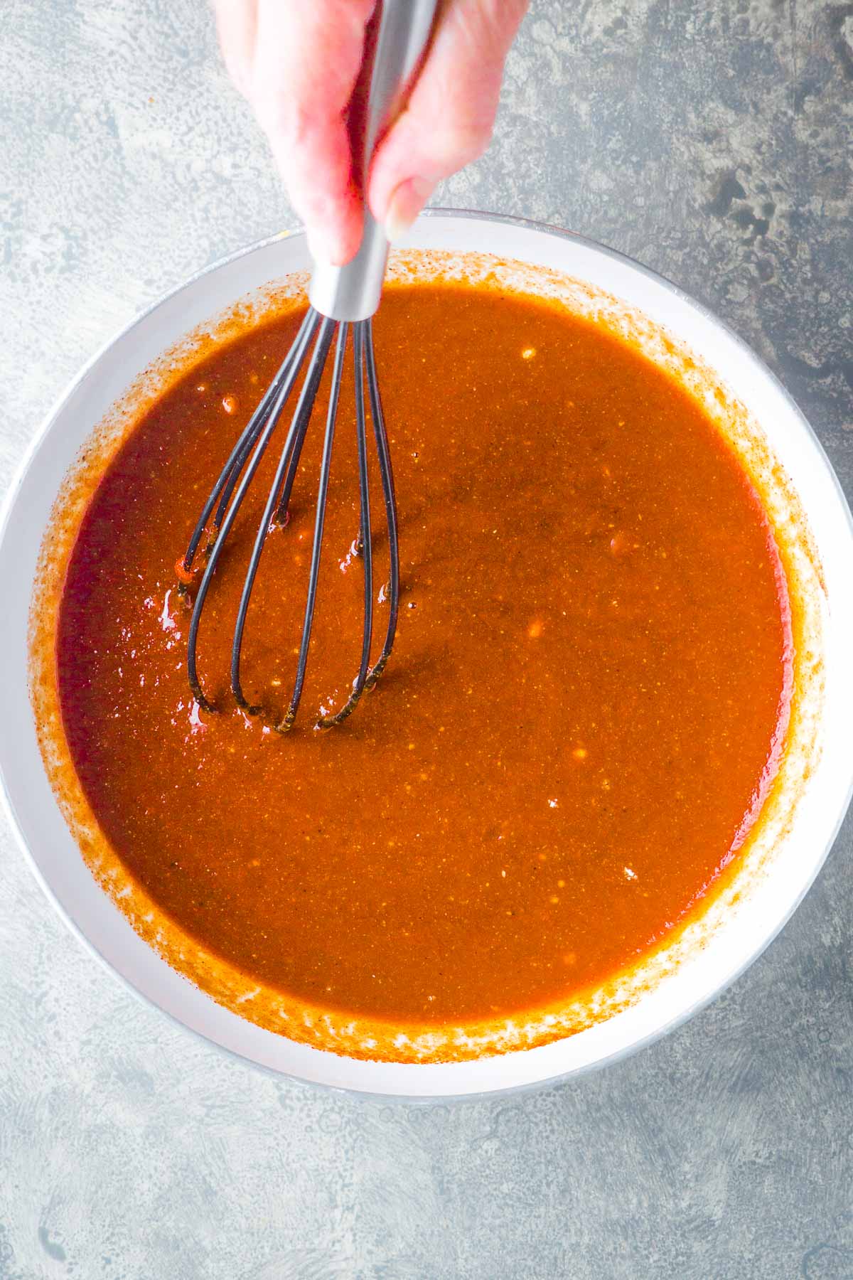 person's hand is whisking bbq sauce in white saucepan
