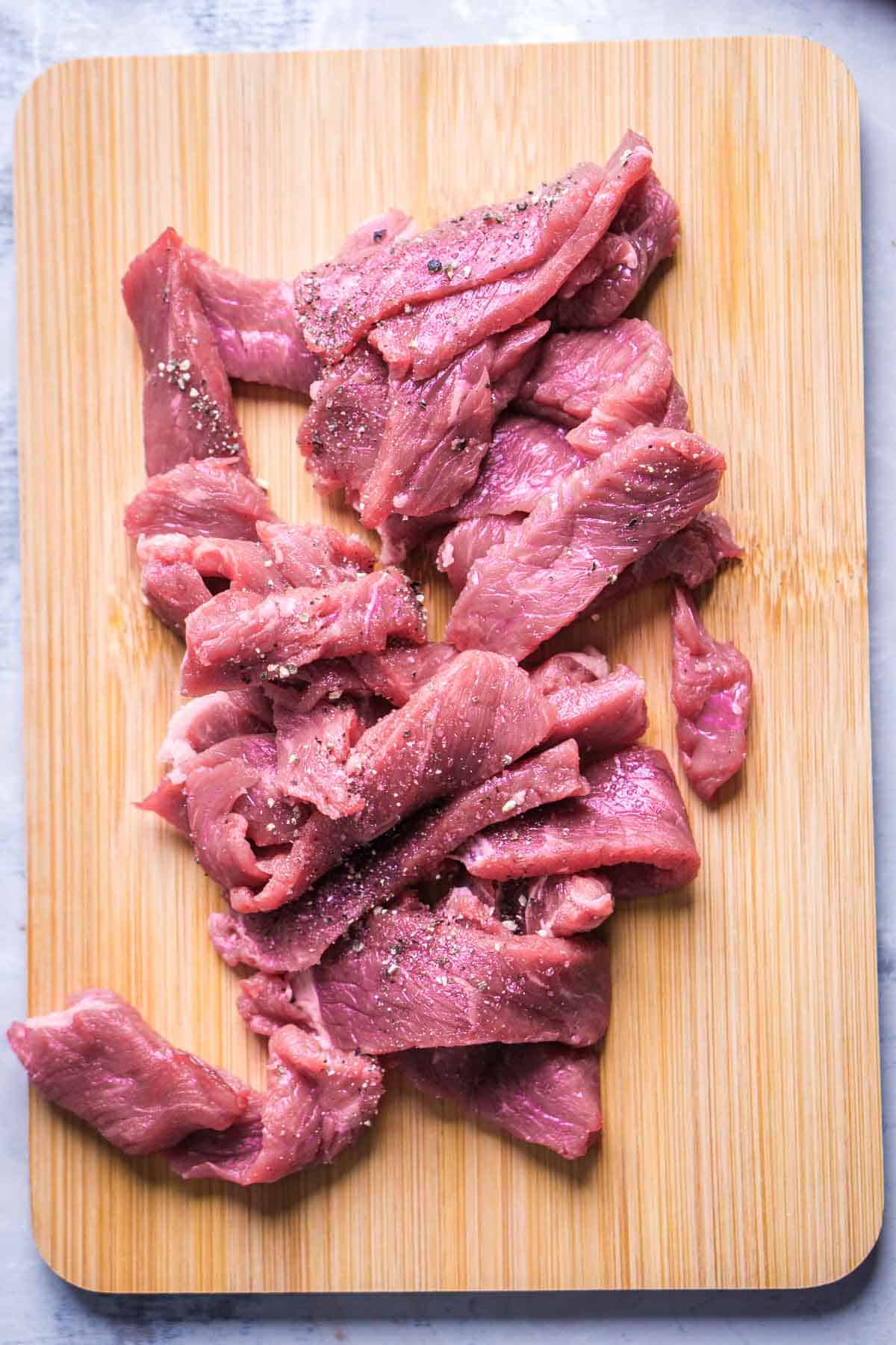 seasoned, thinly sliced beef strips on cutting board