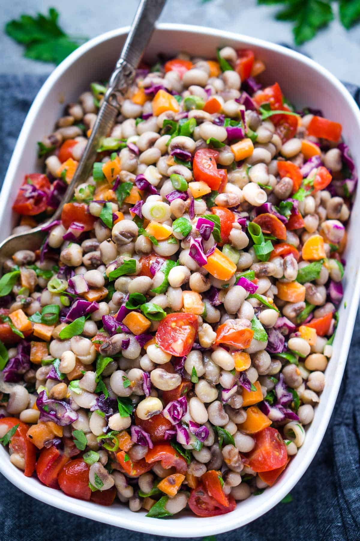 black eyed pea salad in white bowl with serving spoon