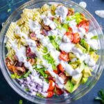 A glass bowl filled with blt pasta salad topped with creamy white dressing.
