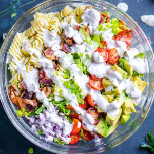 A glass bowl filled with blt pasta salad topped with creamy white dressing.
