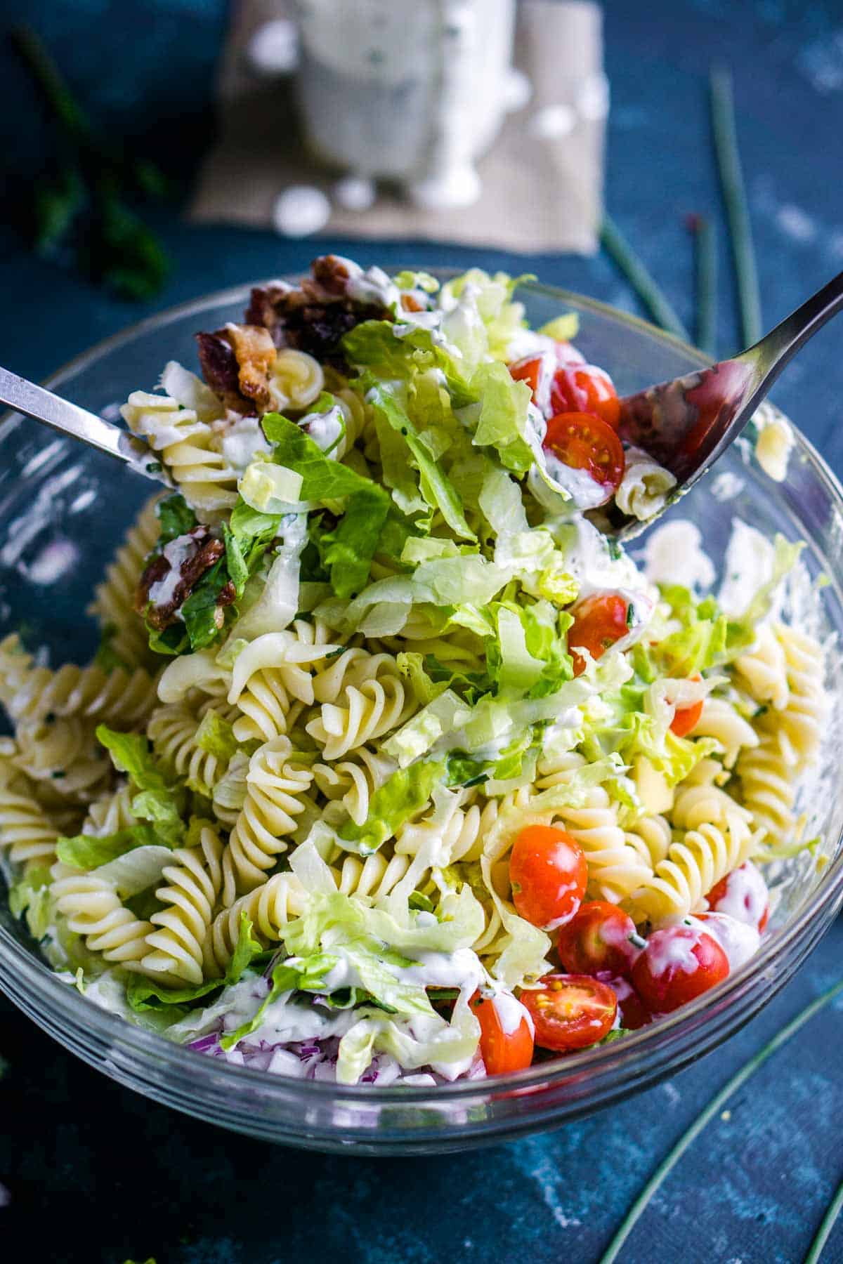 BLT pasta salad in glass bowl is tossed with salad tongs