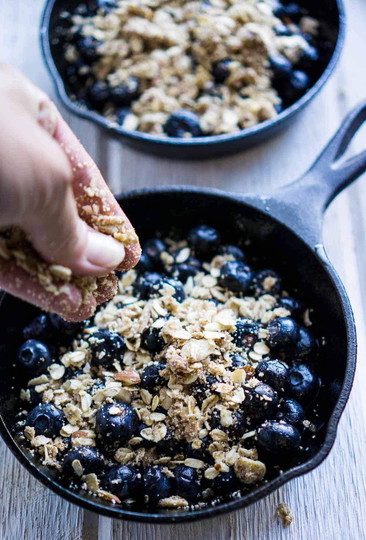 oat topping is sprinkled over blueberries in iron skillet
