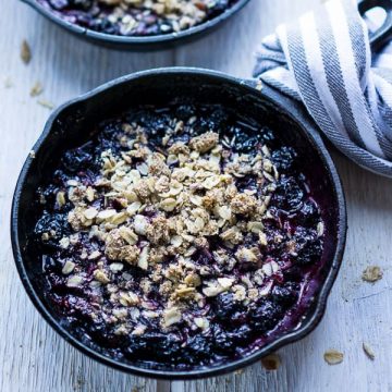 warm blueberry crisp in iron skillet with linen-wrapped handle on white wood surface