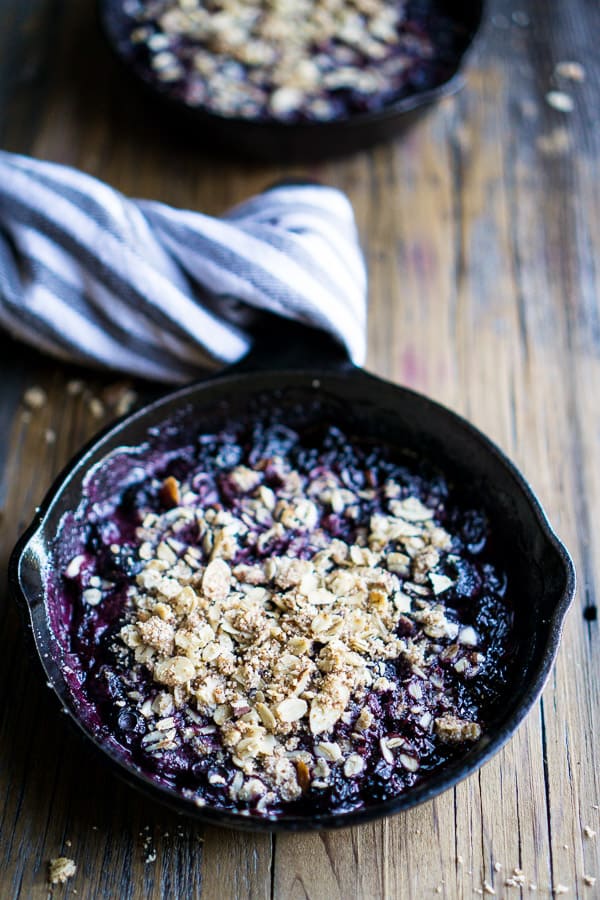warm blueberry crisp in iron skillet with linen-wrapped handle on brown wood surface