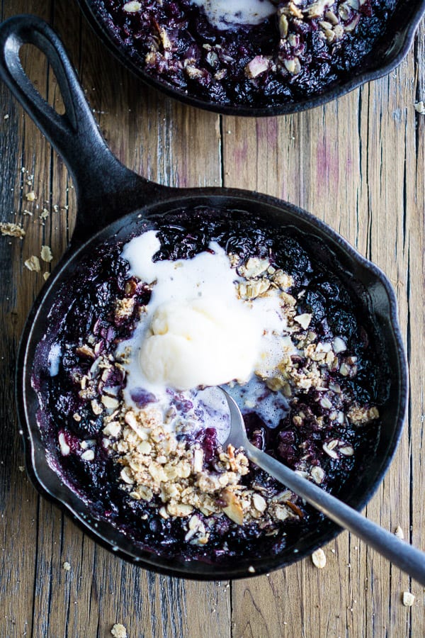 warm blueberry crisp with melted ice cream and spoon in iron skillet on wood surface