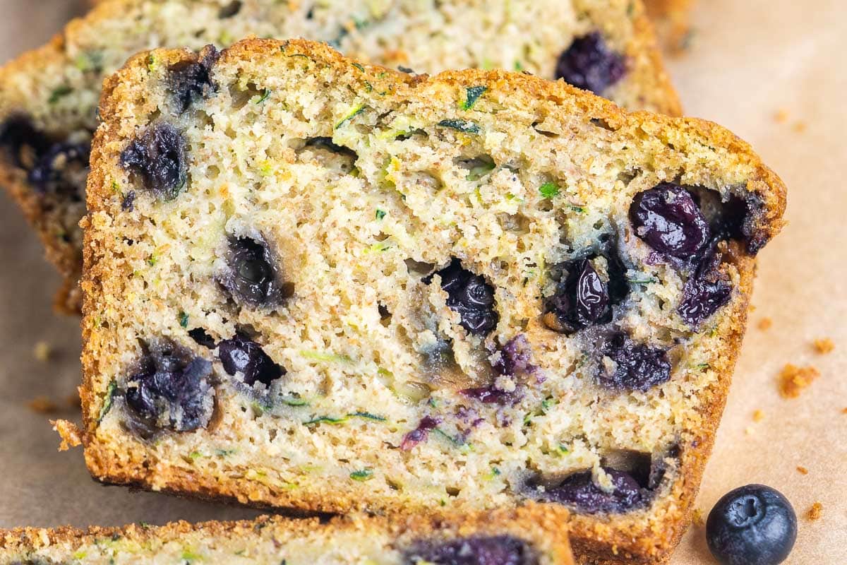 Close-up of sliced blueberry zucchini bread showing visible blueberries and bits of shredded zucchini in the moist, golden-brown crumb.