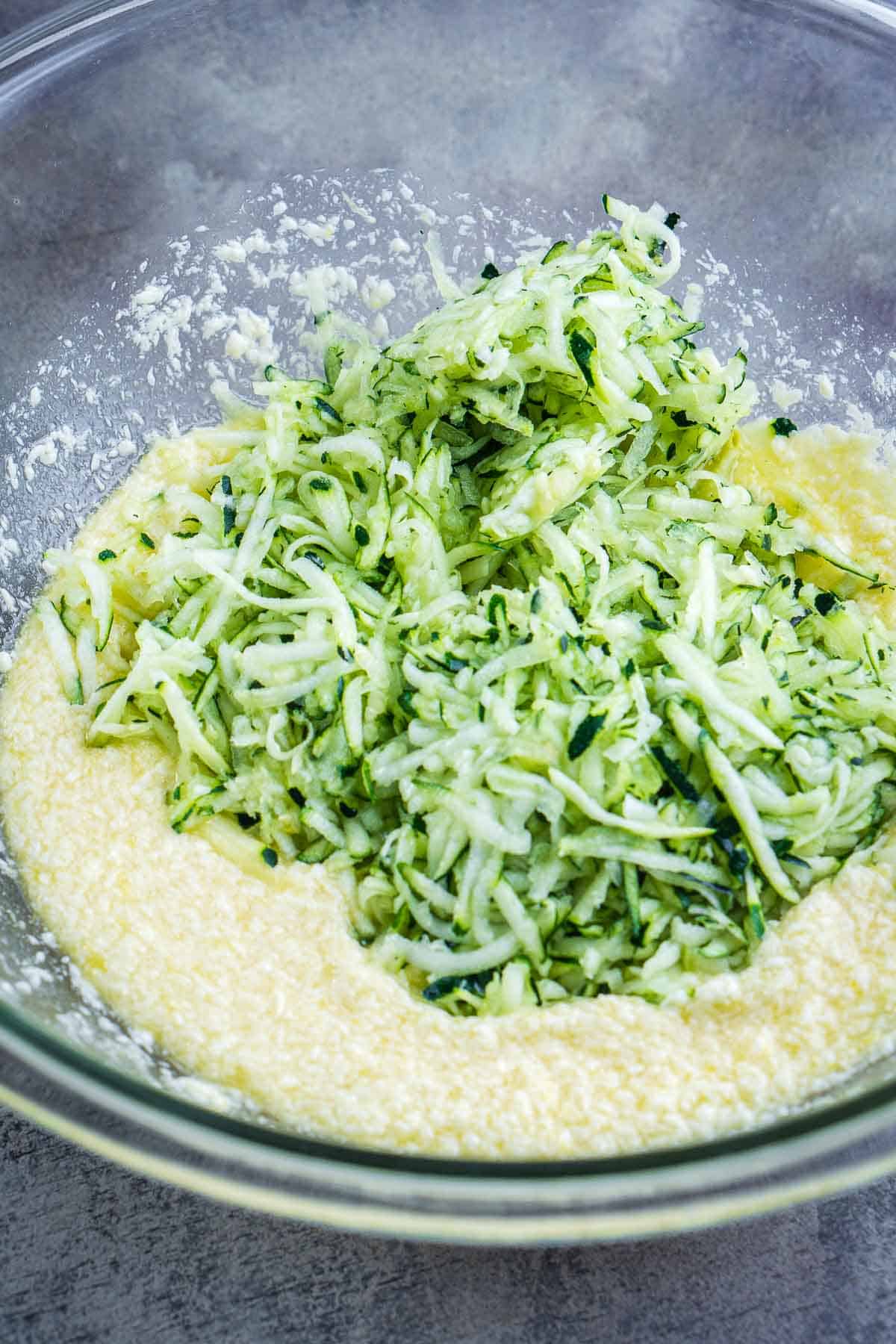 freshly shredded zucchini sits on wet mixture in glass bowl