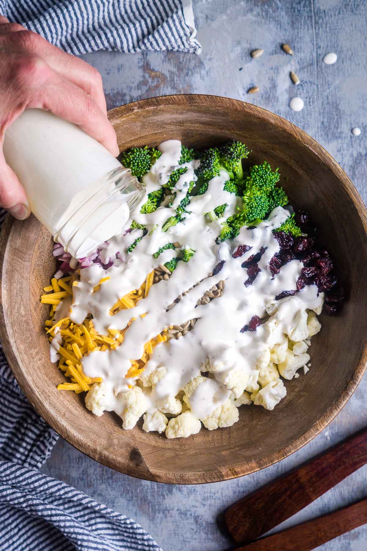 dressing is being poured over cauliflower broccoli salad in wood bowl