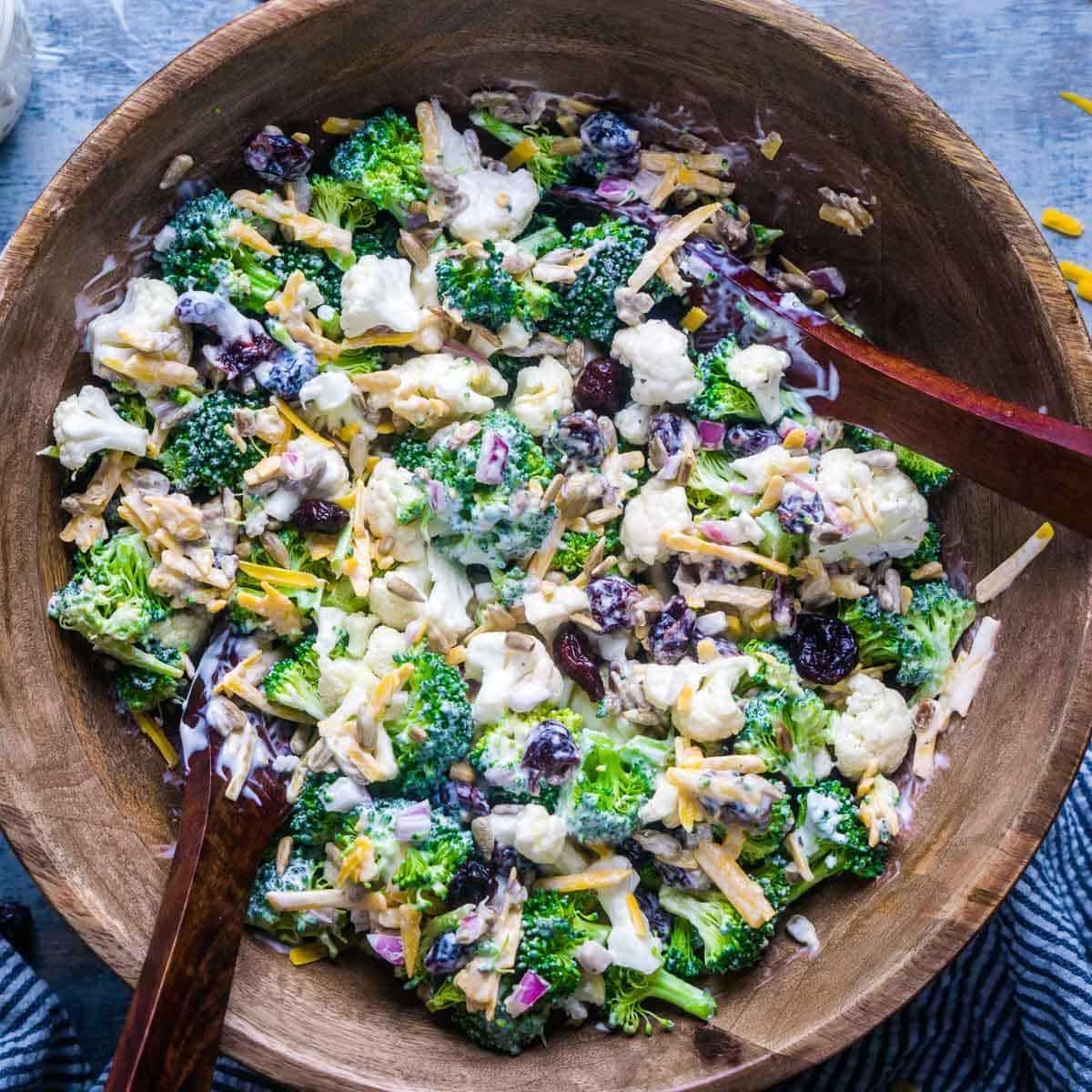 broccoli cauliflower salad in wood bowl with salad serving utensils
