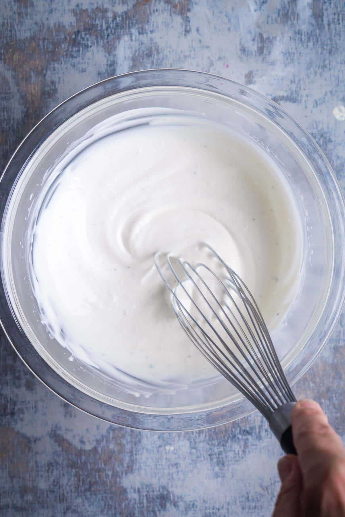 creamy dressing is whisked by hand in glass mixing bowl