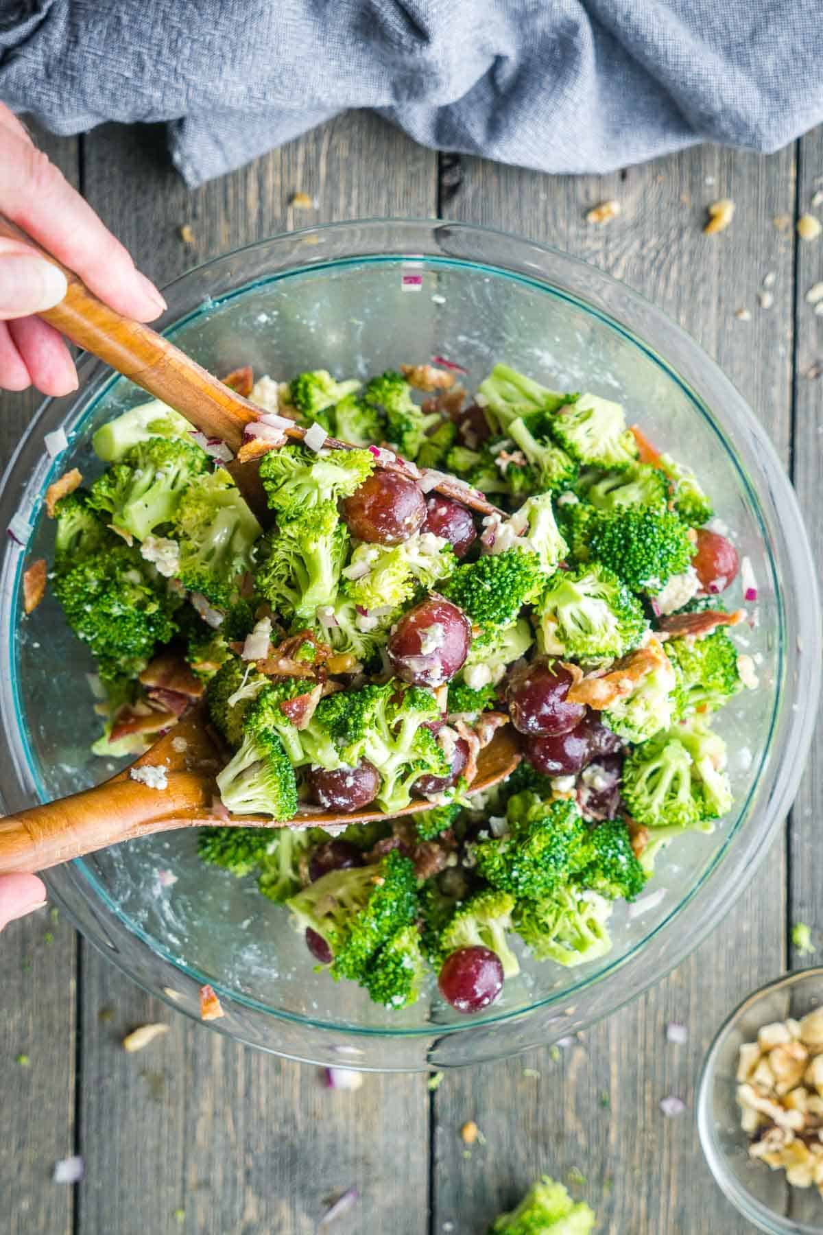 broccoli grape salad is tossed with salad tongs in glass mixing bowl