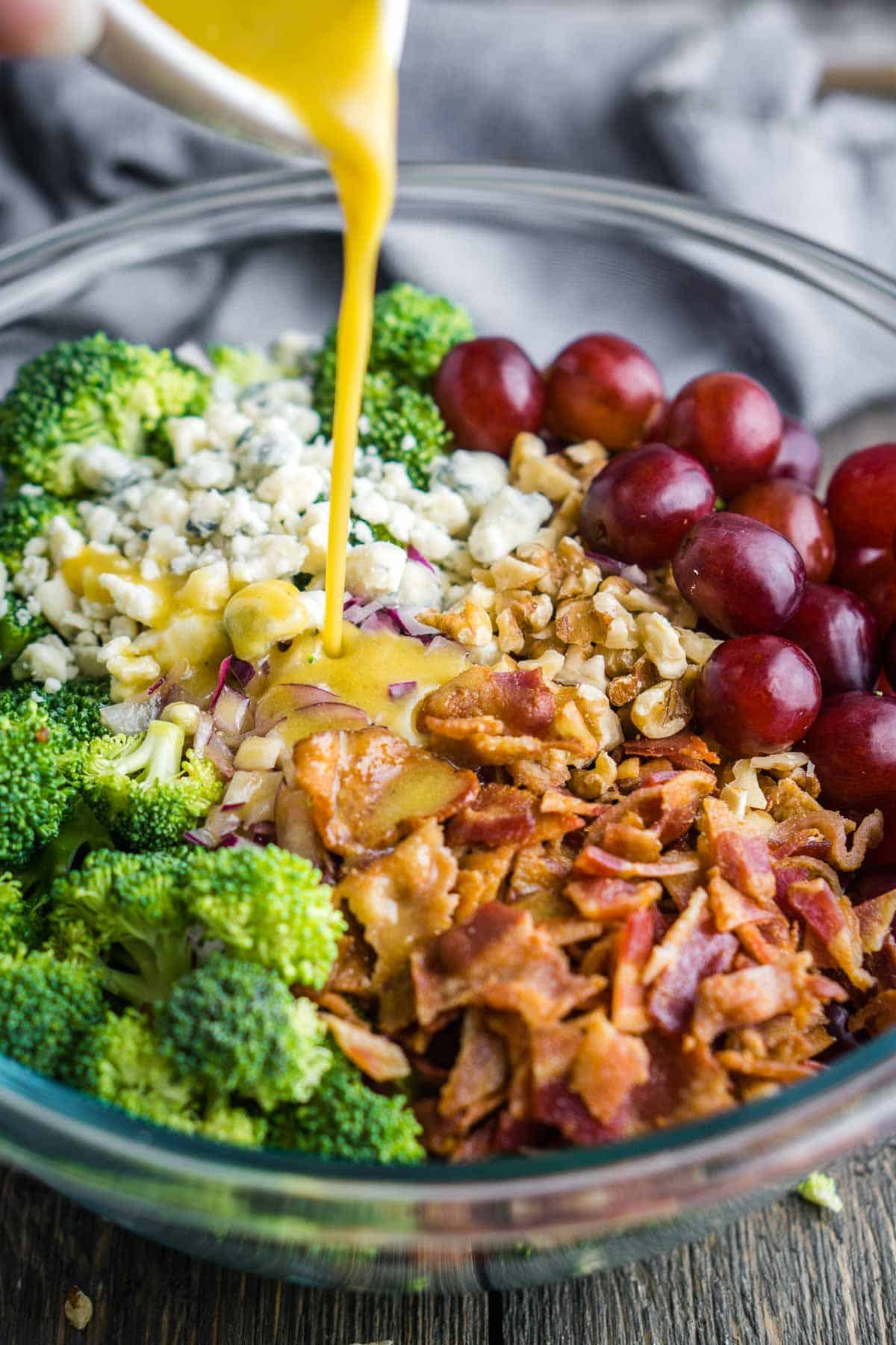 dressing is poured over broccoli grape salad in glass mixing bowl