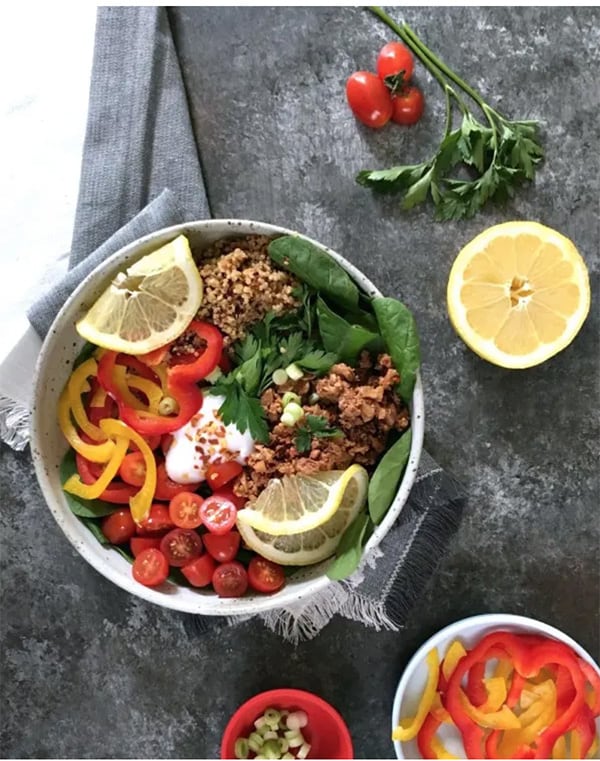 Vegan Deconstructed Stuffed Pepper Bowl ingredients in white bowl next to lemon wedge, parsley, sliced bell peppers, tomatoes, and linen napkin