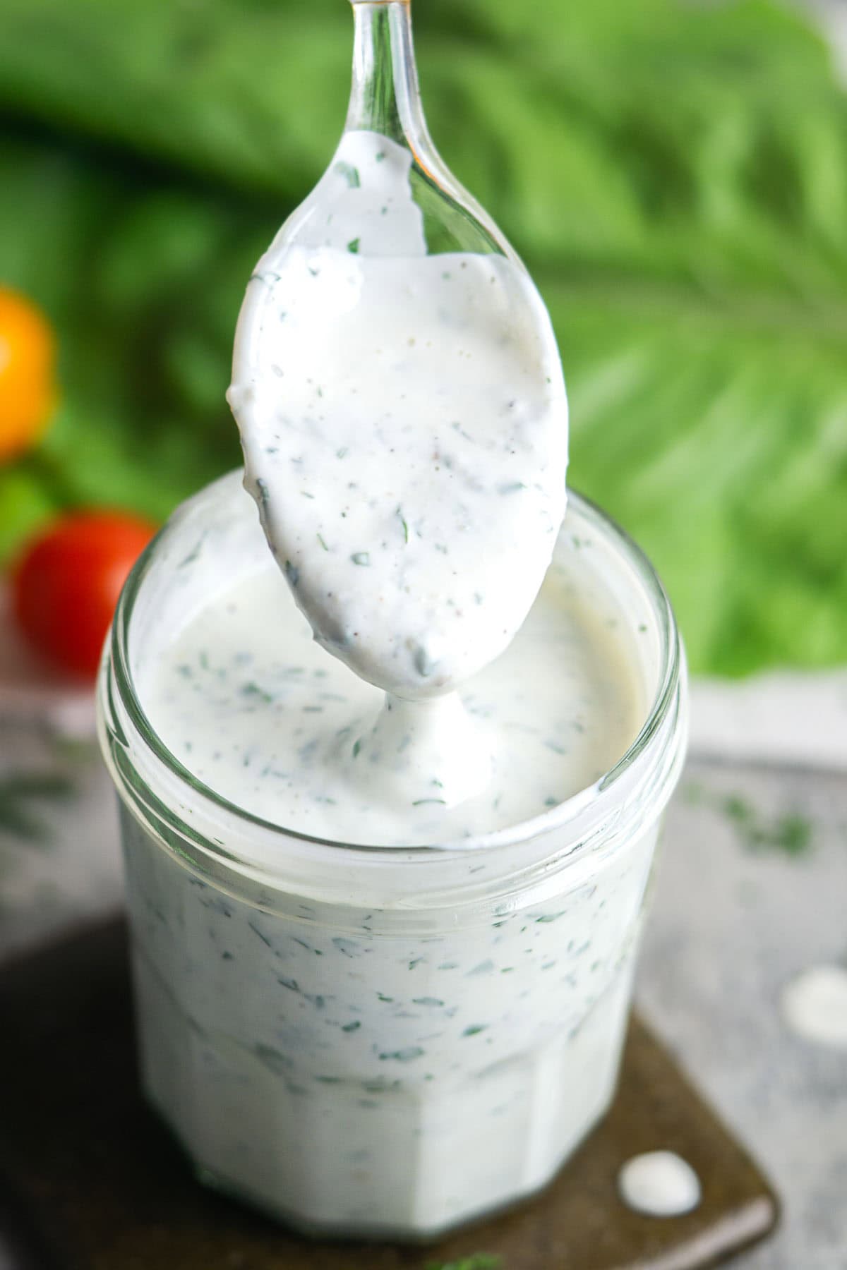 Restaurant-style buttermilk ranch dressing is creamy, quick, and made with simple ingredients. Use fresh herbs or dried herbs for convenience. Rich buttermilk gives this ranch dressing its classic, irresistible flavor. A spoonful of creamy, herb-speckled buttermilk ranch dressing is held above a glass jar filled with the same dressing, with fresh greens and tomatoes in the background.
