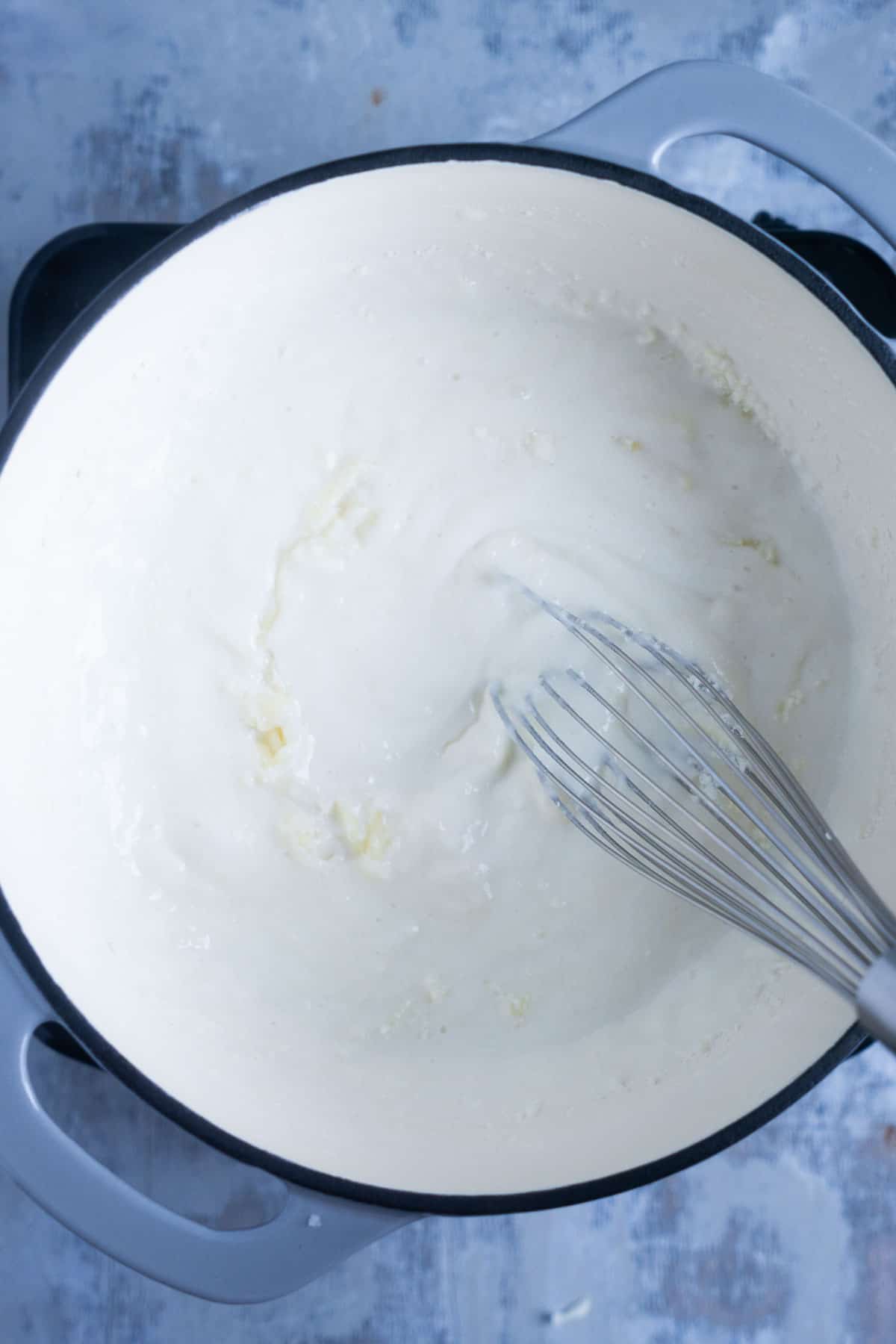 whisk stirs white cheese sauce in saucepan