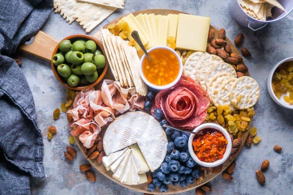 round charcuterie board with sliced meats, cheeses, fruit, nuts, olives, spreads, and crackers