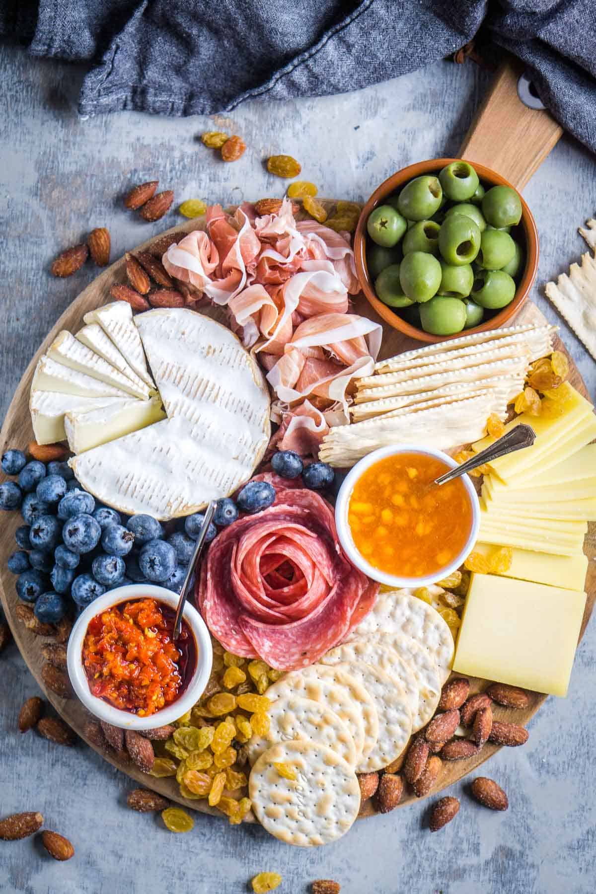 round charcuterie board with sliced meats, cheeses, fruit, nuts, olives, and spreads