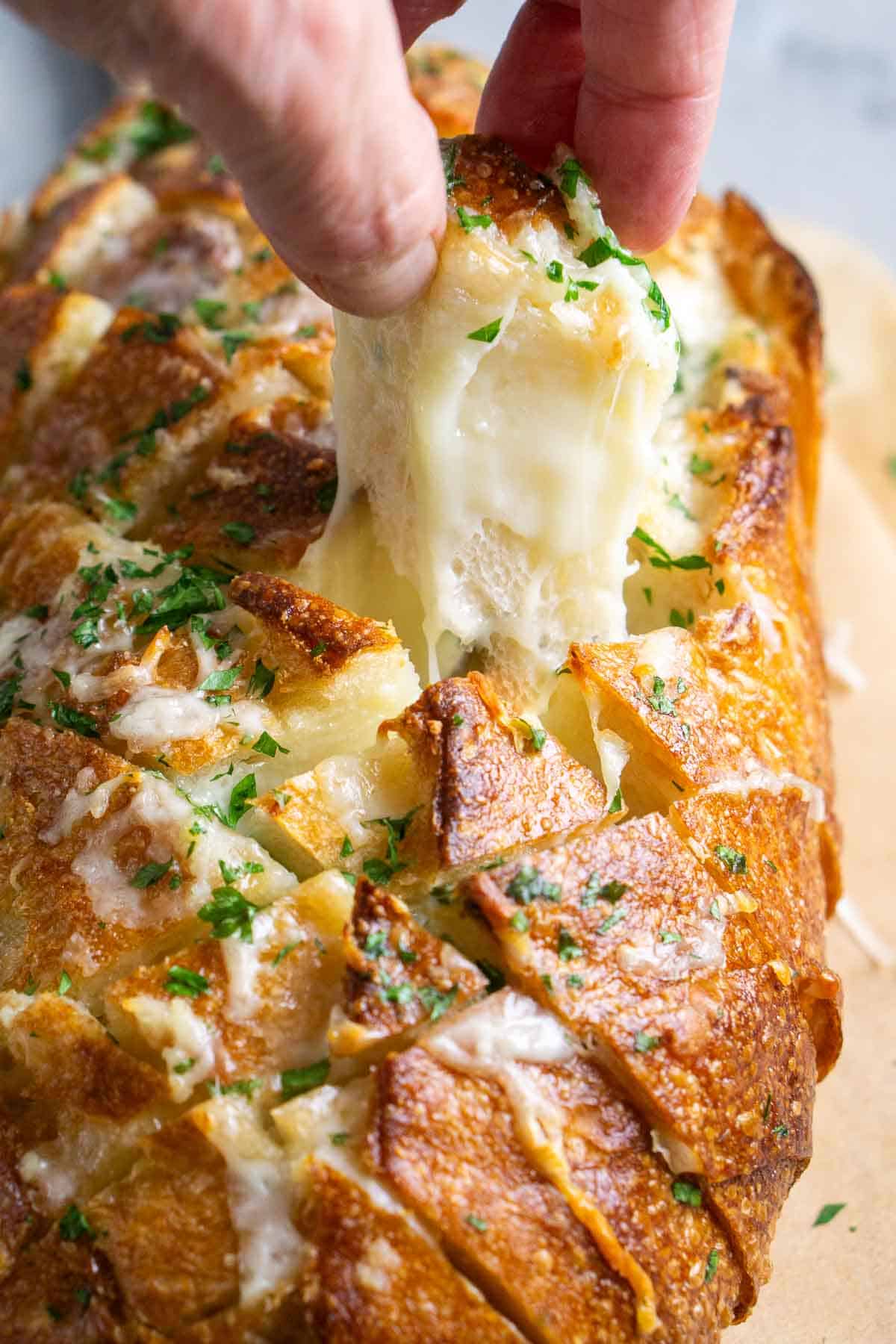 person's hand pulls a bread square from the loaf with a stretchy cheese pull trailing under it