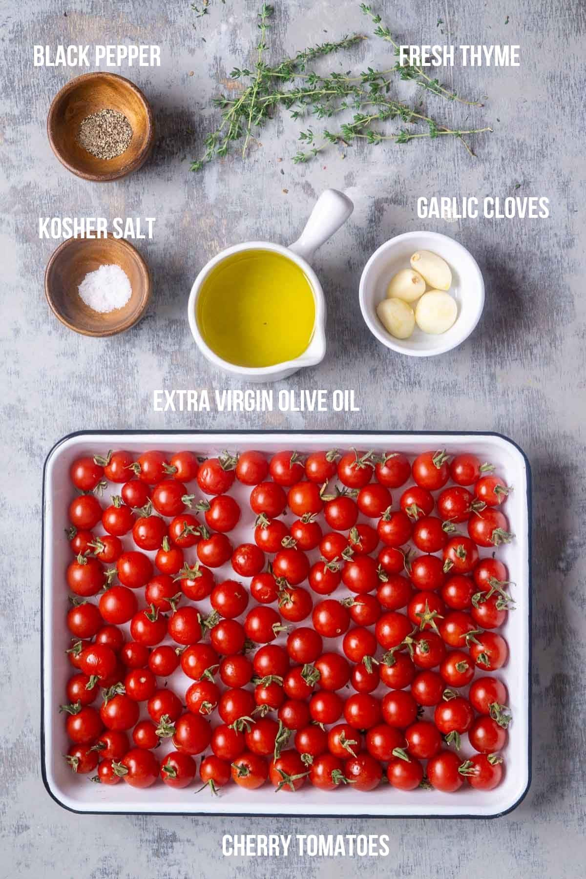 Ingredients for cherry confit laid out and labeled: cherry tomatoes in a dish, olive oil, garlic cloves, fresh thyme, kosher salt, and black pepper in bowls on a gray surface.