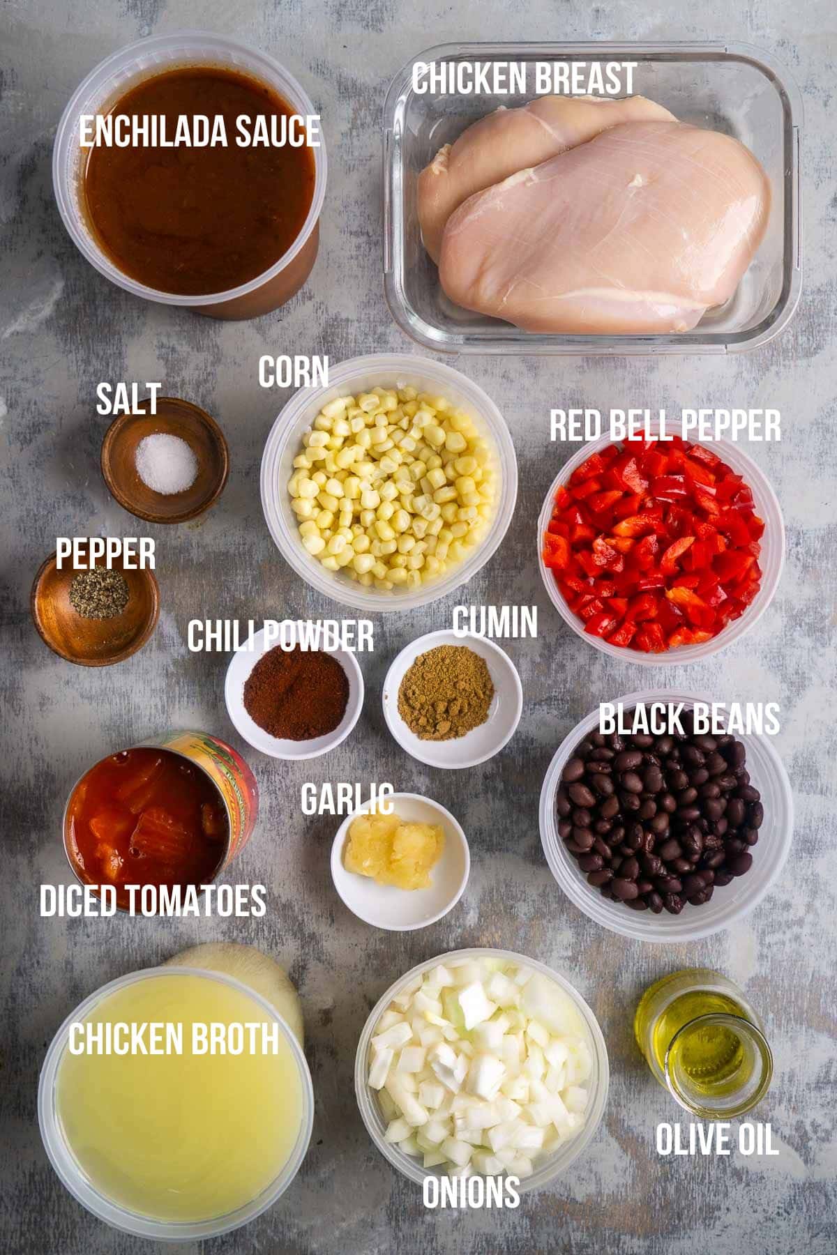 Top view of labeled enchilada soup ingredients: chicken breast, enchilada sauce, salt, pepper, corn, red bell pepper, diced tomatoes, cumin, chili powder, garlic, black beans, chicken broth, onions, olive oil.