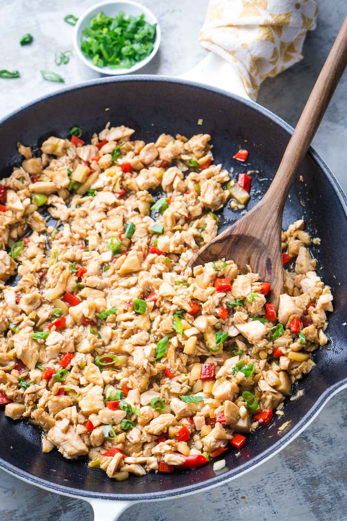 A skillet filled with the cooked filling for chicken lettuce wraps consisting of chopped chicken, mixed with red bell peppers, green onions, and a wooden spoon for stirring.
