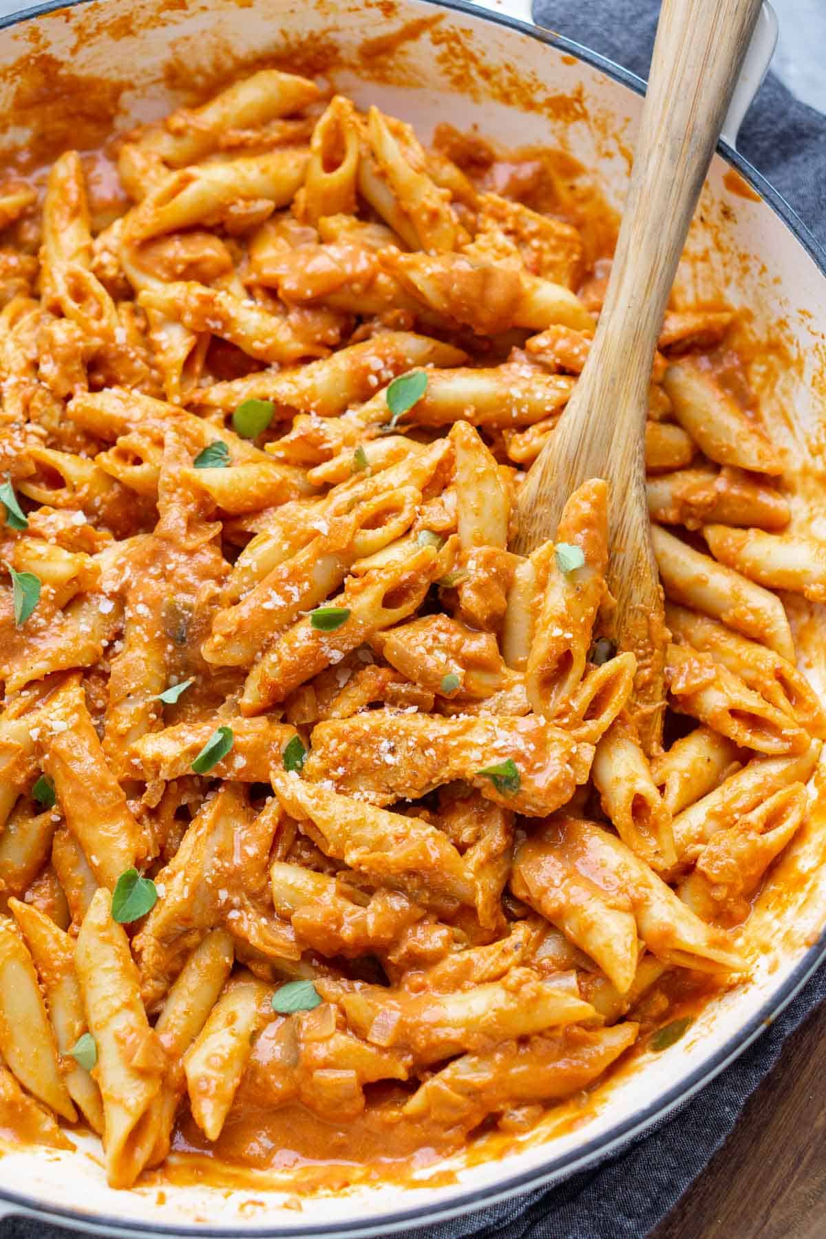 wooden spoon scoops penne alla vodka with chicken in white skillet