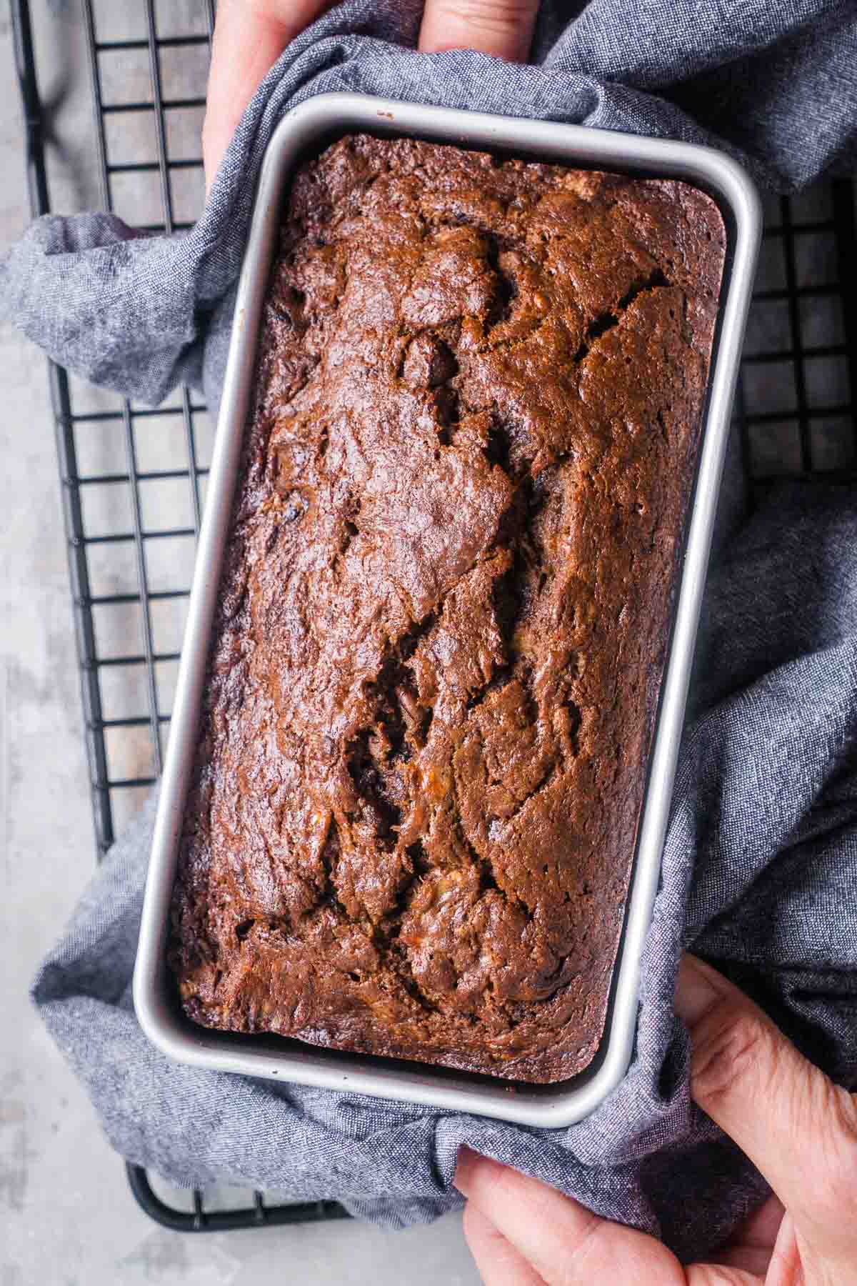 Person's hands set chocolate banana bread loaf on cooling rack