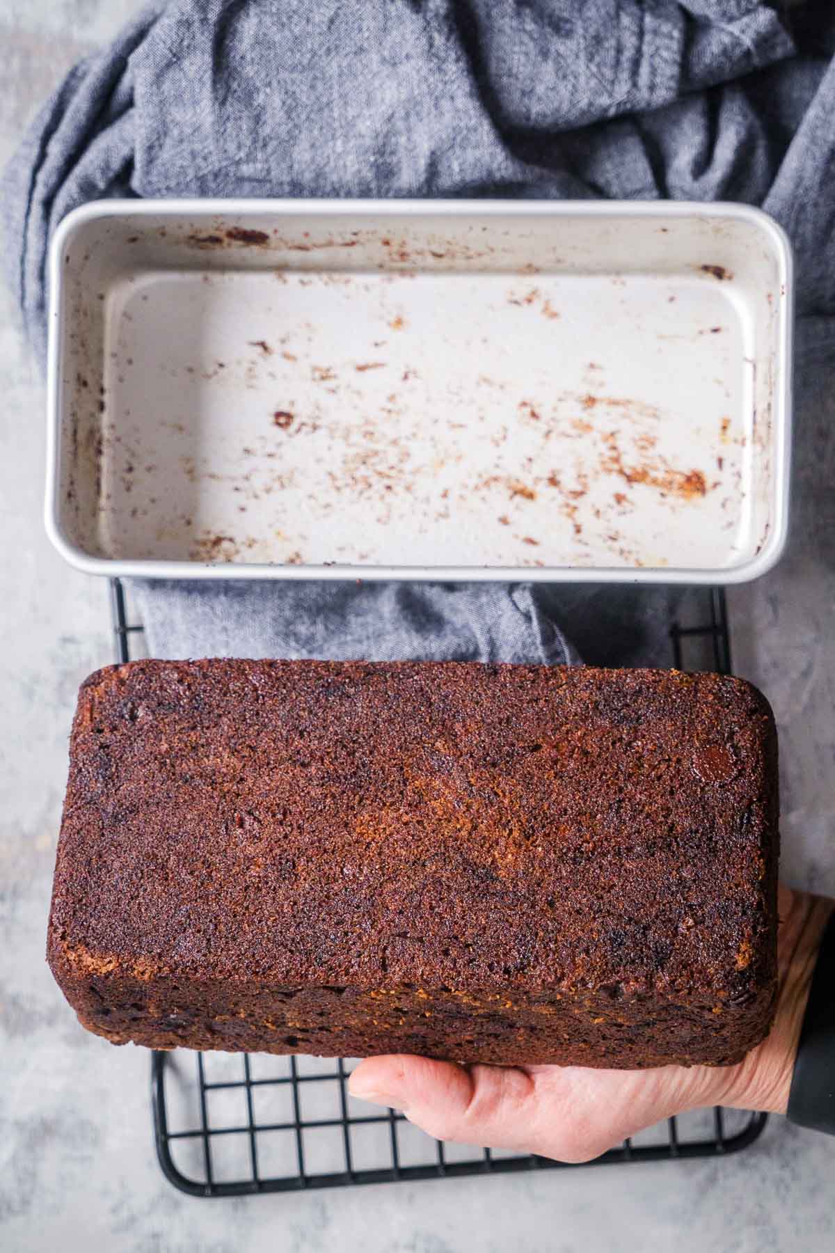 person's hand holding chocolate banana bread loaf that has been released from the loaf pan