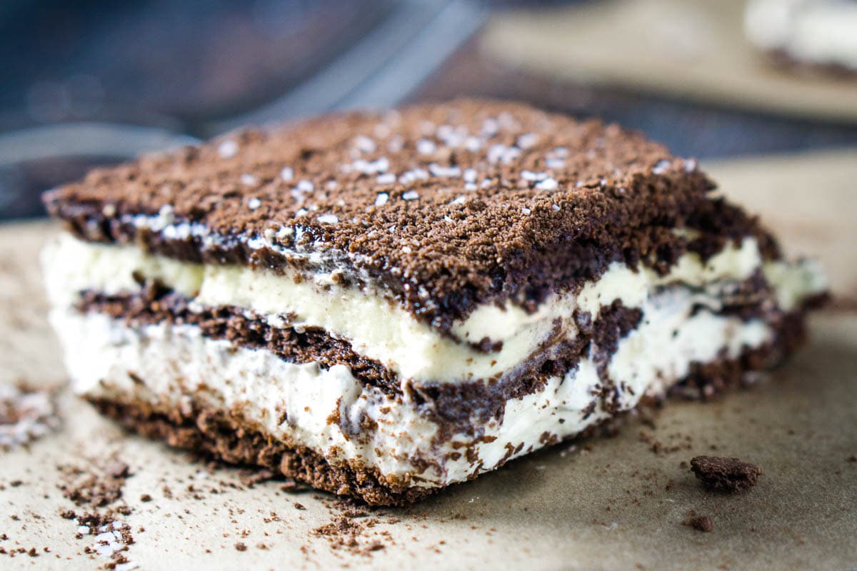 A close-up of a chocolate eclair cake made with chocolate graham cracker and pudding layers with a dusting on top and a sprinkle of flaky sea sat.