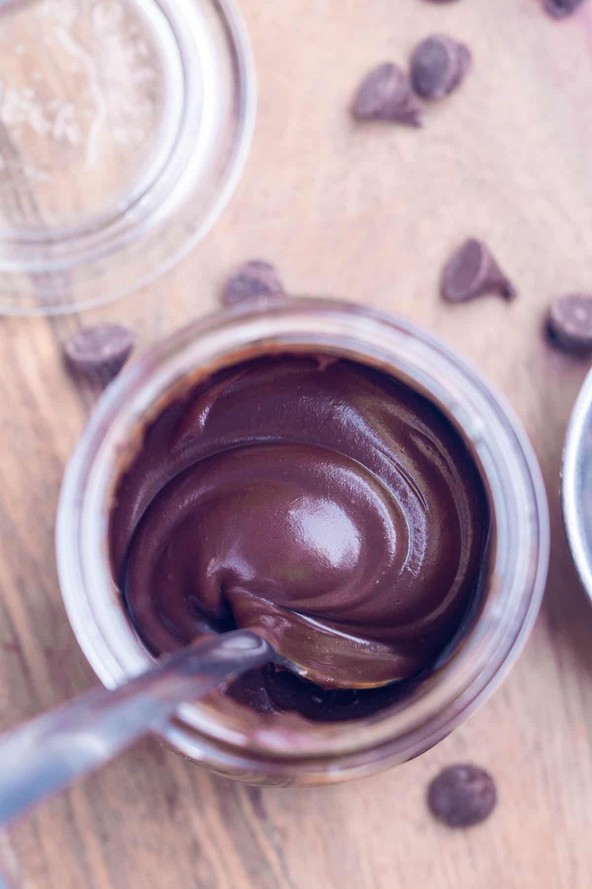 spoon stirring chocolate ganache in glass jar