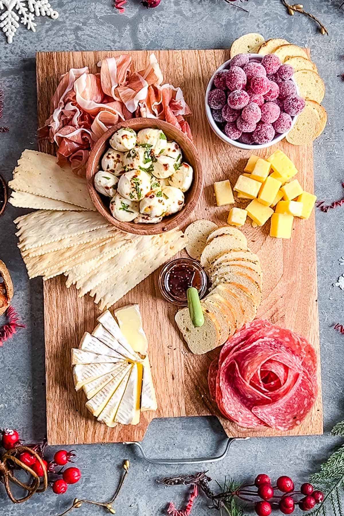 Christmas charcuterie board with cheeses, salami rose, folded proscuitto, sugared cranberries, crackers, and bagel chips