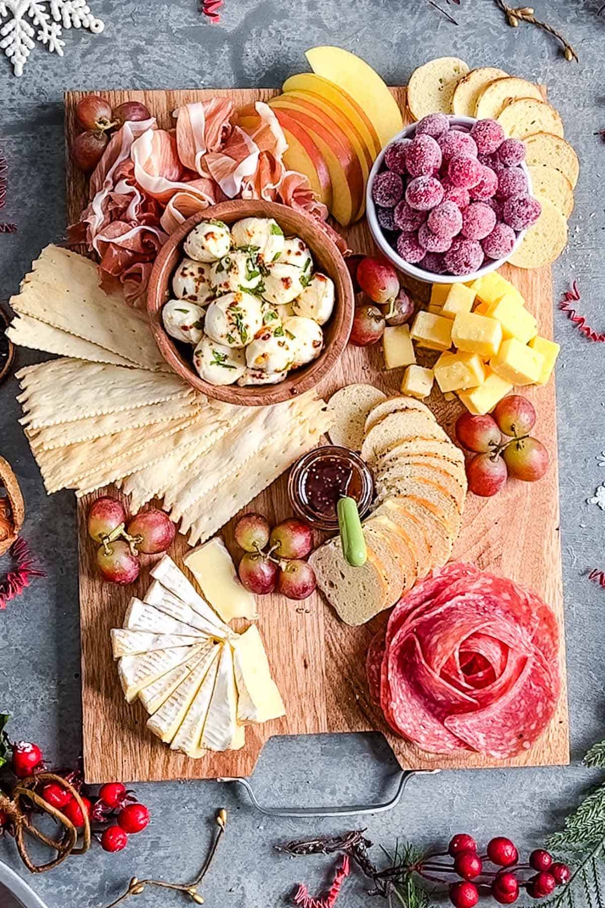 Christmas charcuterie board with 3 cheeses, salami rose, folded proscuitto, sugared cranberries, apple slices, and red grapes