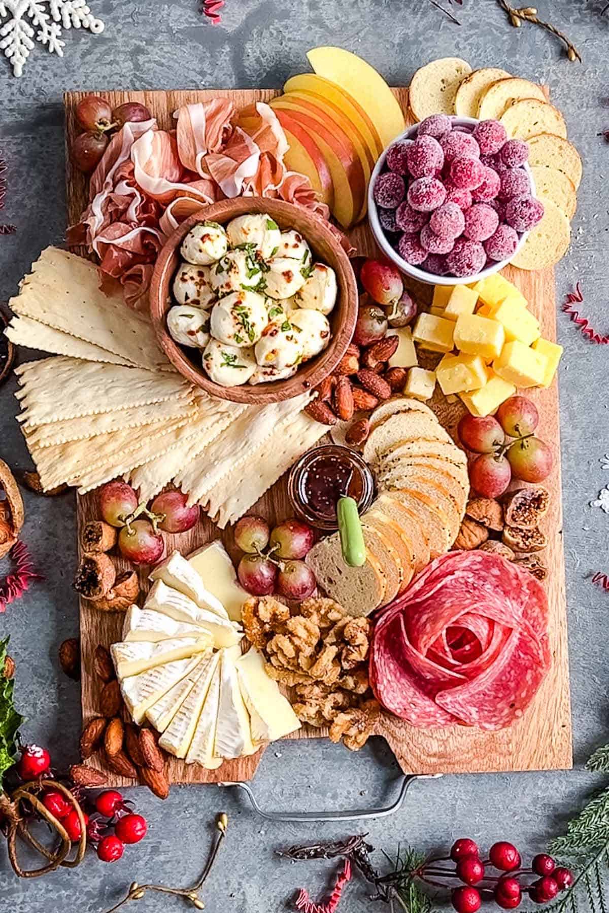 Christmas charcuterie board with 3 cheeses, salami rose, folded proscuitto, sugared cranberries, apple slices, red grapes, walnuts, almonds, and dried figs