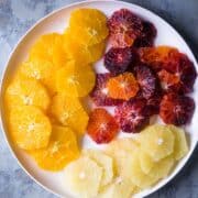 white plate with sliced blood oranges, naval oranges, and white grapefruit