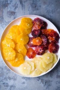 white plate with sliced blood oranges, naval oranges, and white grapefruit