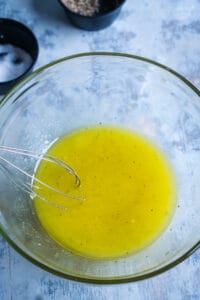 lemon dressing is whisked in glass mixing bowl
