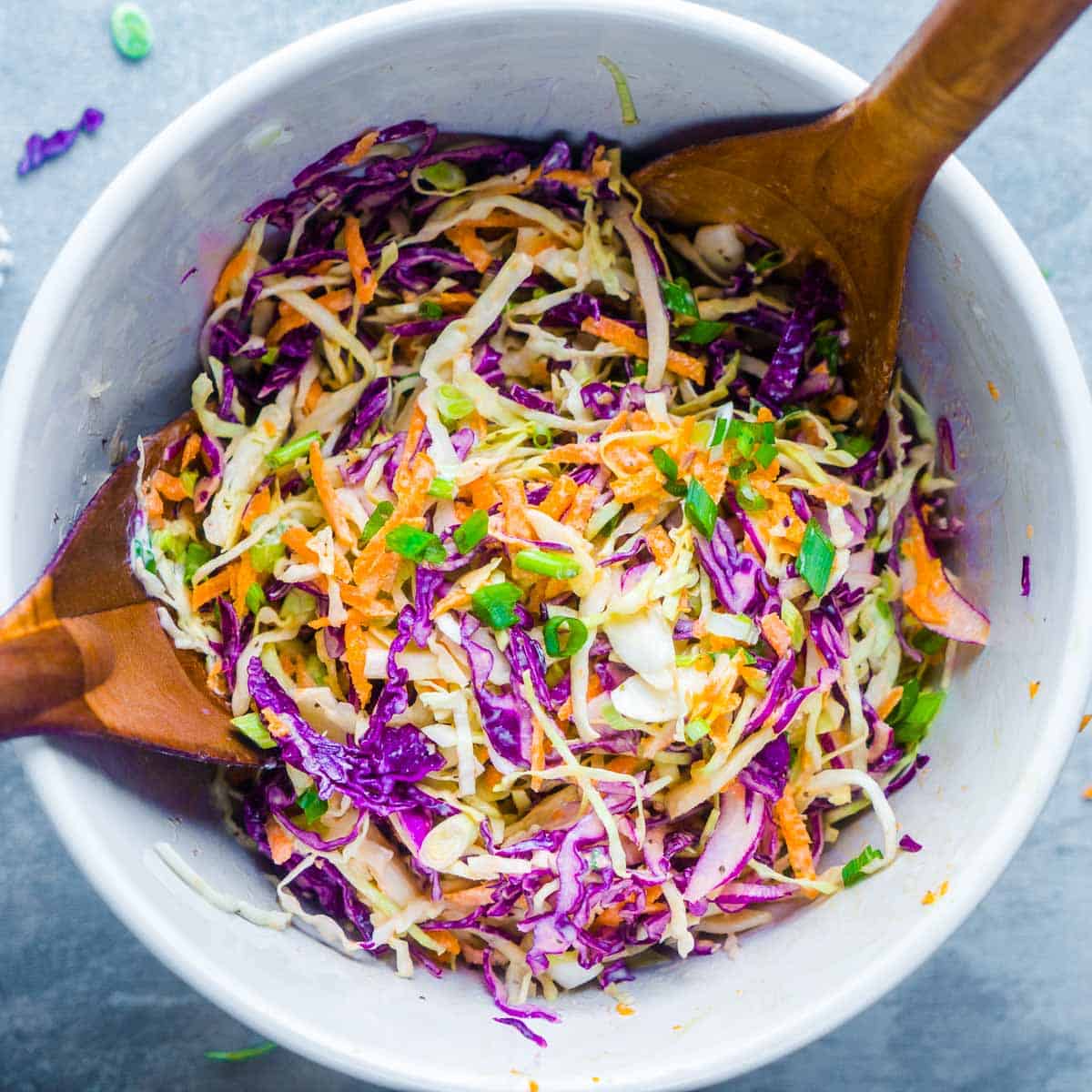 creamy coleslaw in white bowl with wood salad serving utensils