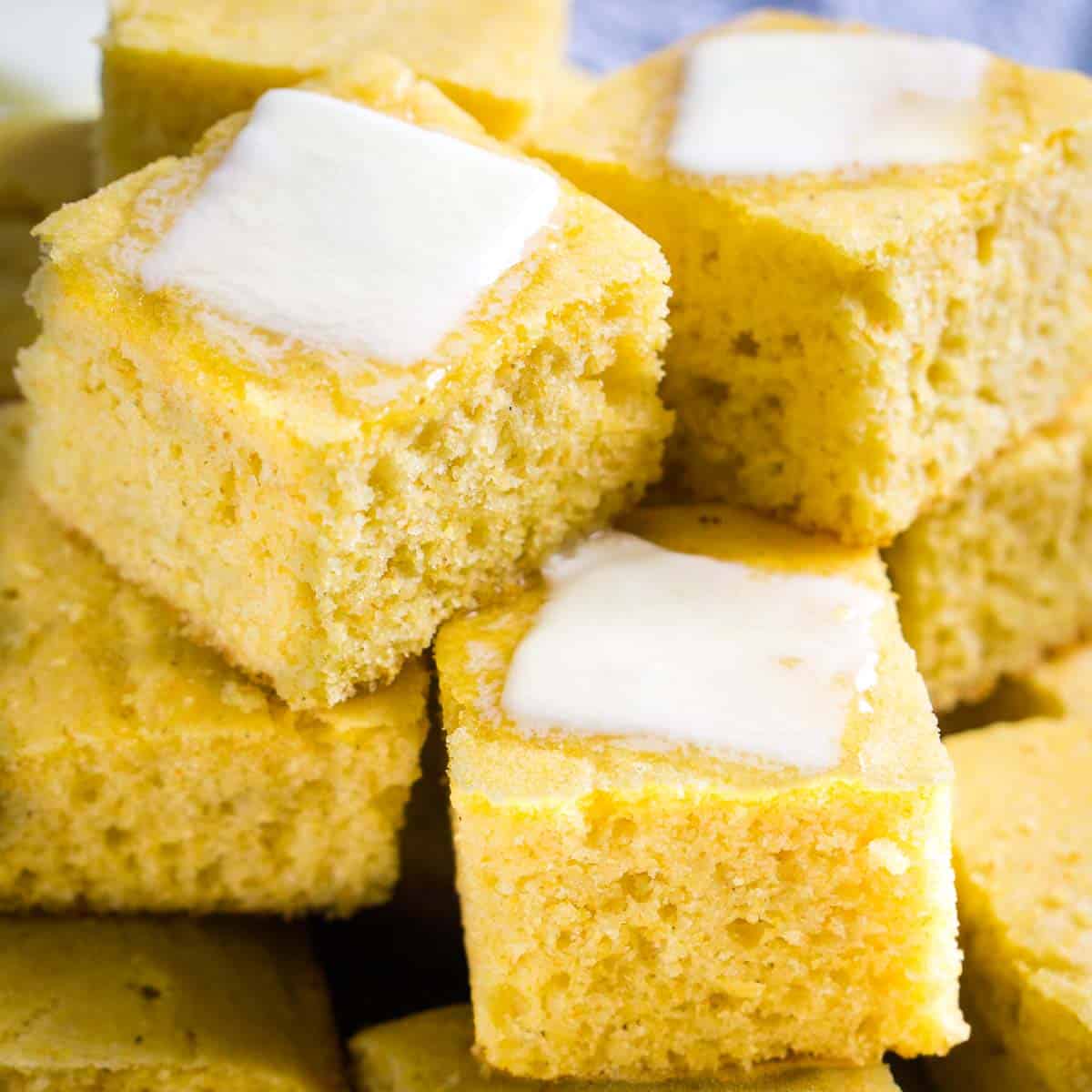 stack of yellow fluffy cornbread squares with melting butter pat on top pieces