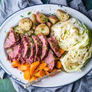 sliced corned beef and cabbage with potatoes and carrots on white serving platter