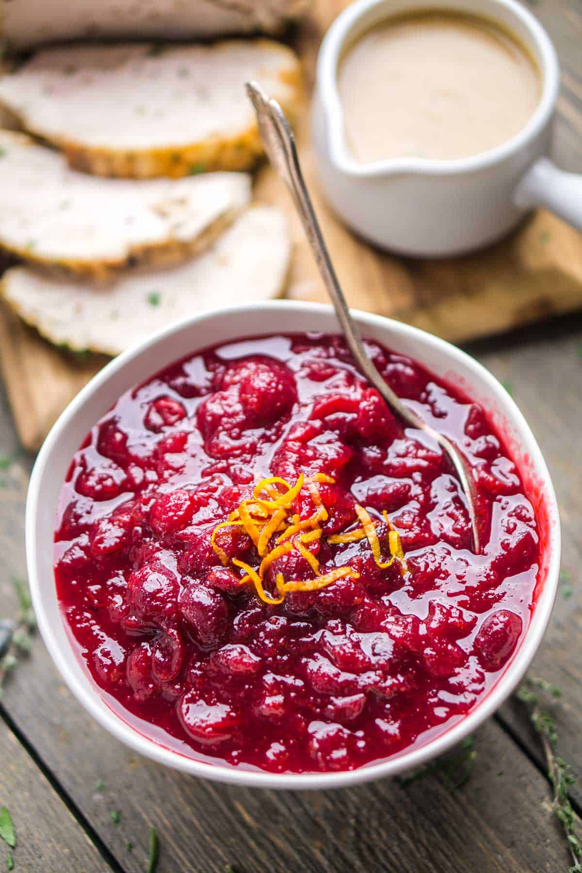 cranberry orange sauce in bowl with serving spoon next to Thanksgiving turkey