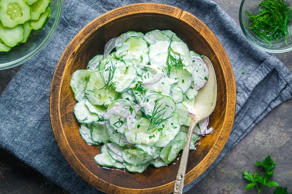 creamy cucumber salad with serving spoon in wood bowl on blue linen