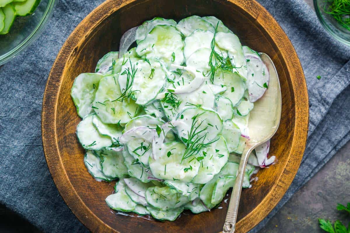 creamy cucumber salad with serving spoon in wood bowl on blue linen