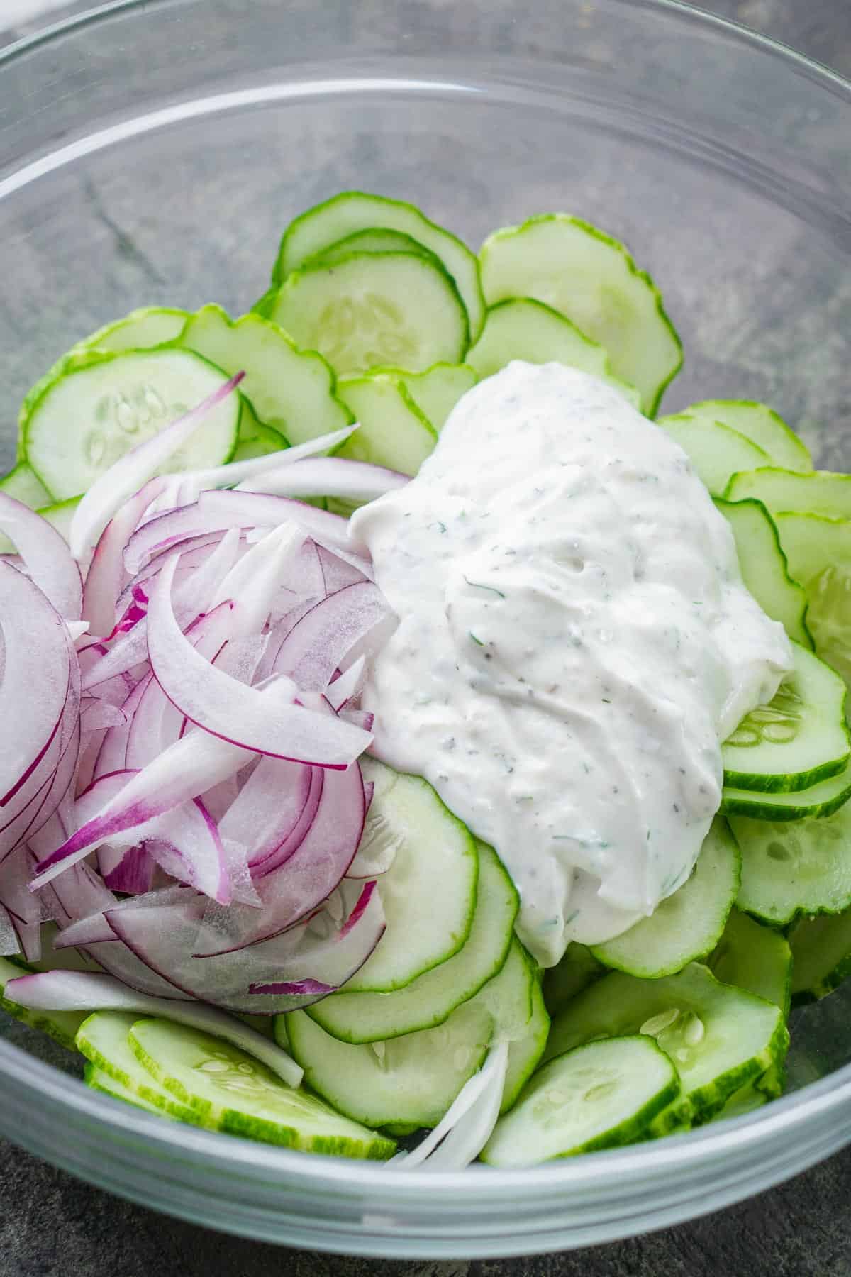 sliced cucumbers, red onions, and cucumber dressing in glass bowl